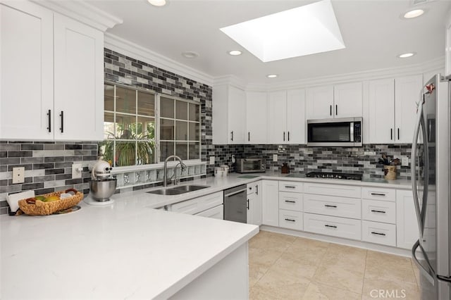 kitchen with a skylight, stainless steel appliances, light countertops, white cabinets, and a sink