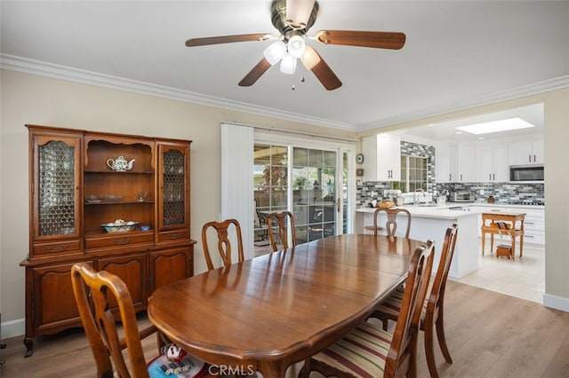 dining room featuring a skylight, baseboards, ceiling fan, ornamental molding, and light wood-type flooring