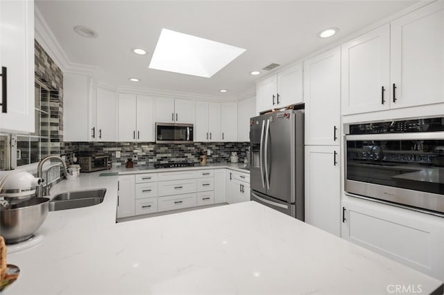 kitchen featuring appliances with stainless steel finishes, a skylight, a sink, and white cabinetry