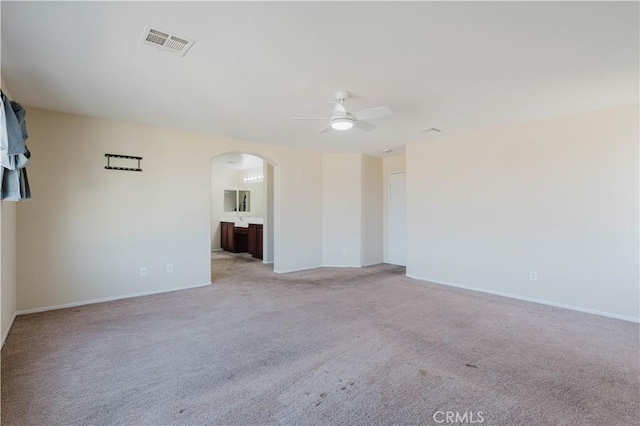 spare room featuring light carpet, ceiling fan, visible vents, and arched walkways