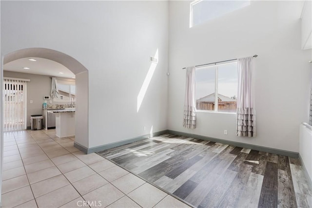 empty room featuring a towering ceiling, light wood finished floors, baseboards, and arched walkways