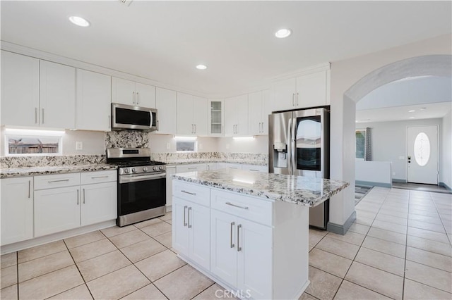 kitchen featuring light tile patterned floors, stainless steel appliances, arched walkways, and white cabinets