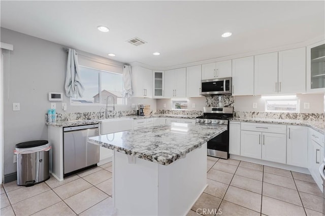 kitchen with visible vents, a center island, stainless steel appliances, white cabinetry, and a sink