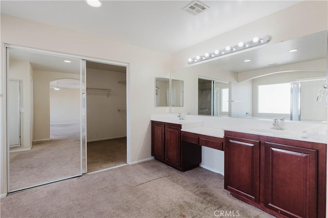 bathroom with visible vents, baseboards, double vanity, carpet, and a walk in closet