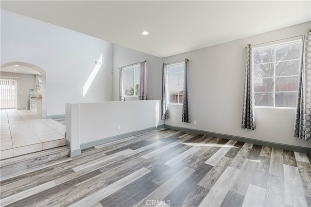 unfurnished room featuring arched walkways, baseboards, recessed lighting, and wood finished floors