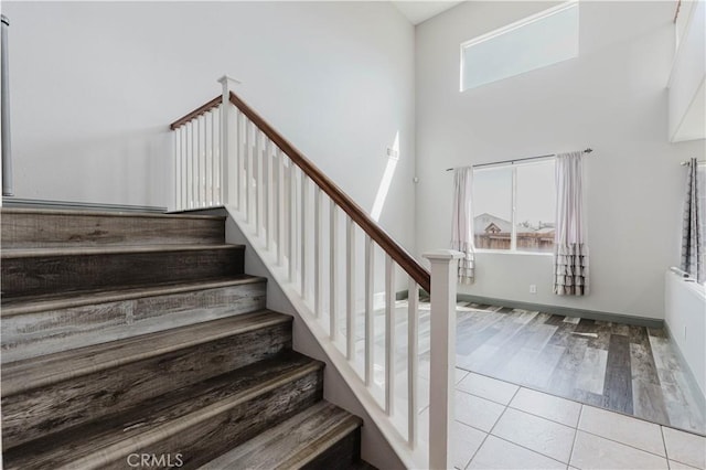 staircase with tile patterned flooring, a towering ceiling, and baseboards