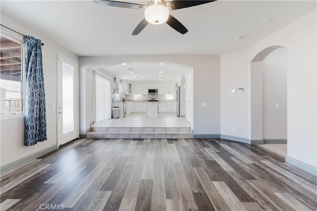 unfurnished living room featuring a ceiling fan, light wood-style flooring, arched walkways, and baseboards