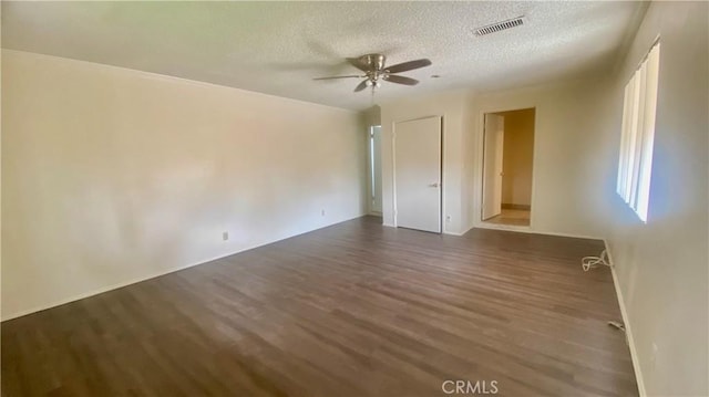 empty room featuring dark wood-style floors, a textured ceiling, visible vents, and a ceiling fan