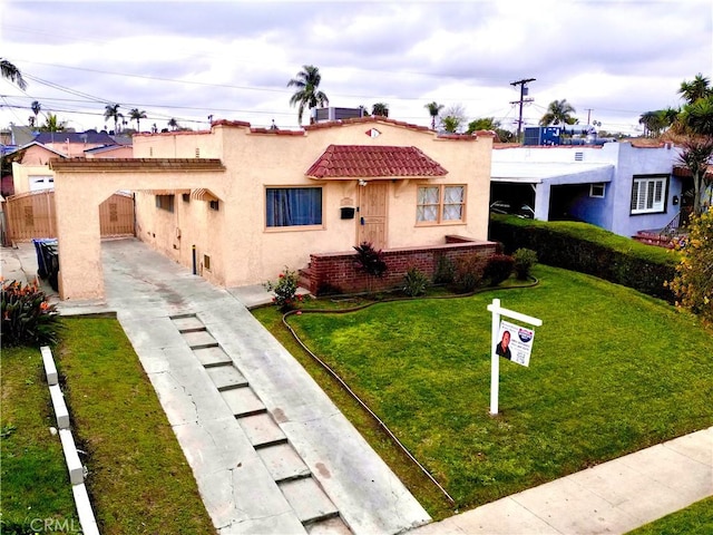 mediterranean / spanish home featuring brick siding, a front lawn, fence, a tiled roof, and stucco siding