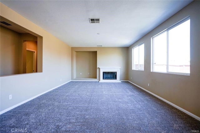 unfurnished living room with carpet floors, a glass covered fireplace, visible vents, and baseboards