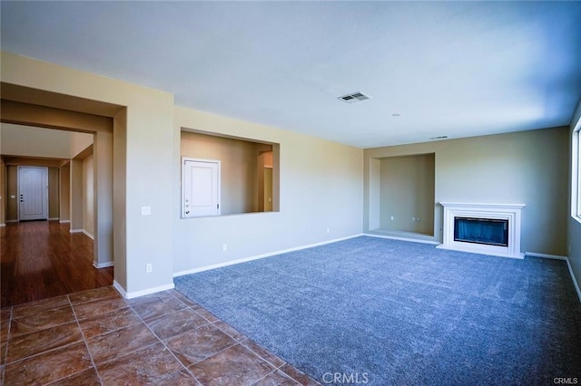 unfurnished living room with a glass covered fireplace, baseboards, visible vents, and dark colored carpet