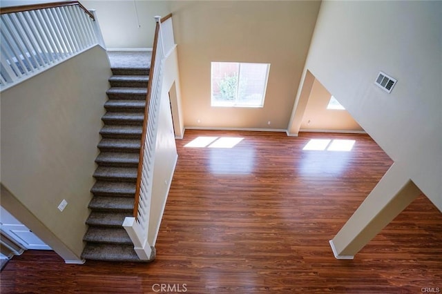 staircase with a towering ceiling, baseboards, visible vents, and wood finished floors