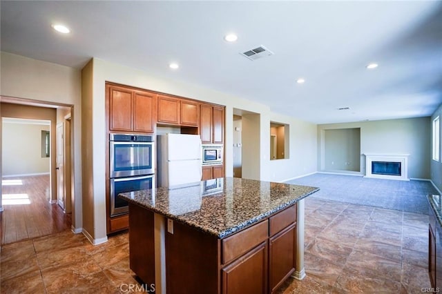 kitchen featuring a kitchen island, visible vents, appliances with stainless steel finishes, dark stone countertops, and a glass covered fireplace