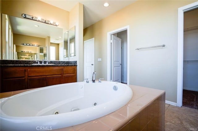 bathroom with a walk in closet, vanity, a whirlpool tub, baseboards, and tile patterned floors