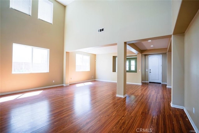 unfurnished living room with baseboards, a high ceiling, visible vents, and dark wood-style flooring