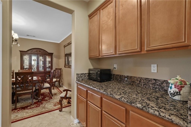 kitchen with visible vents, dark stone counters, ornamental molding, brown cabinets, and black microwave