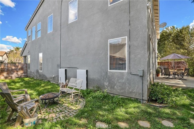 rear view of property featuring an outdoor fire pit, stucco siding, fence, and a patio