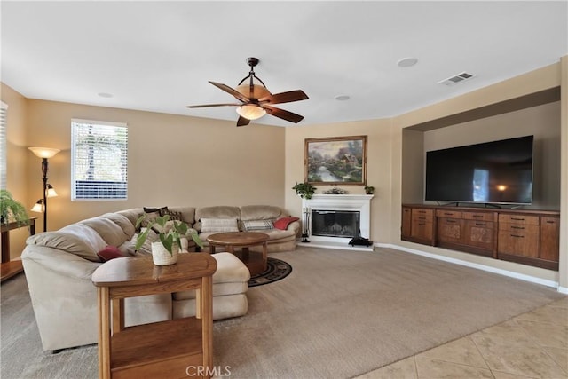 living room with light tile patterned floors, visible vents, a ceiling fan, light colored carpet, and a glass covered fireplace