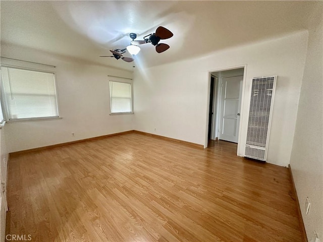 unfurnished room with a ceiling fan, light wood-type flooring, a heating unit, and baseboards