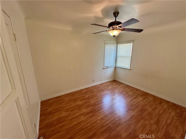 empty room with wood finished floors, a ceiling fan, and baseboards