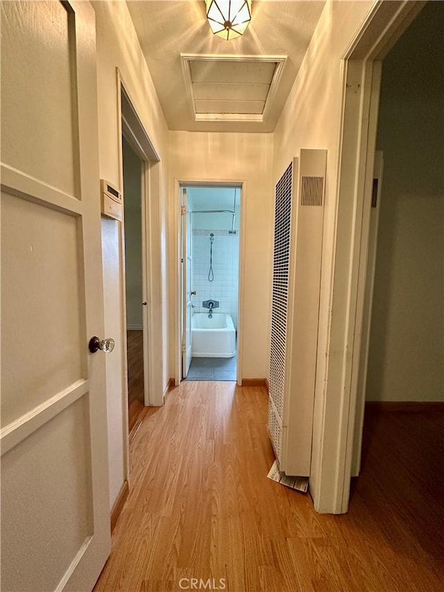 hallway with attic access, a heating unit, baseboards, and wood finished floors