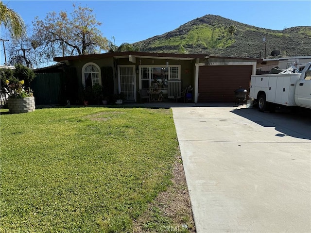 ranch-style home with concrete driveway, a front lawn, an attached garage, and a mountain view