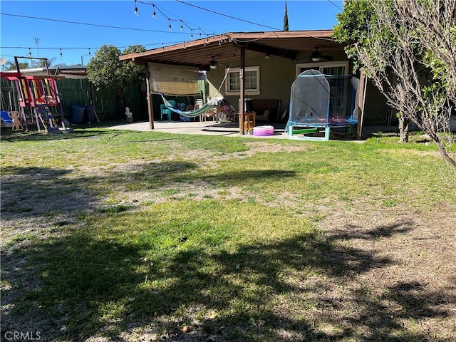 view of yard featuring ceiling fan, a trampoline, fence, a patio area, and a playground