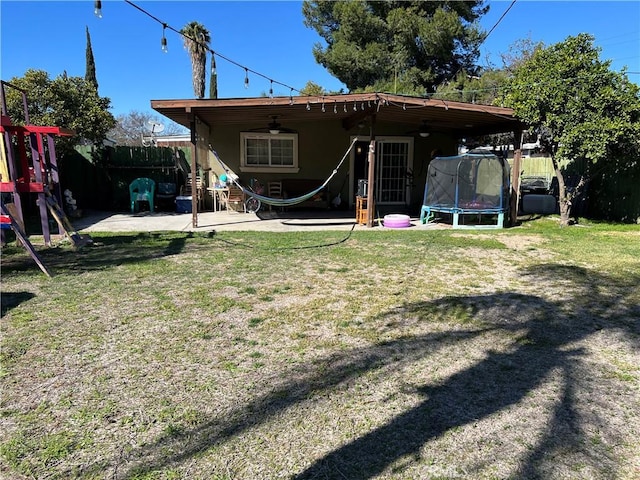 back of property with a patio, a playground, fence, a yard, and a trampoline