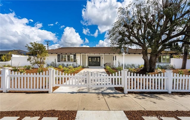 ranch-style house featuring a fenced front yard and stucco siding