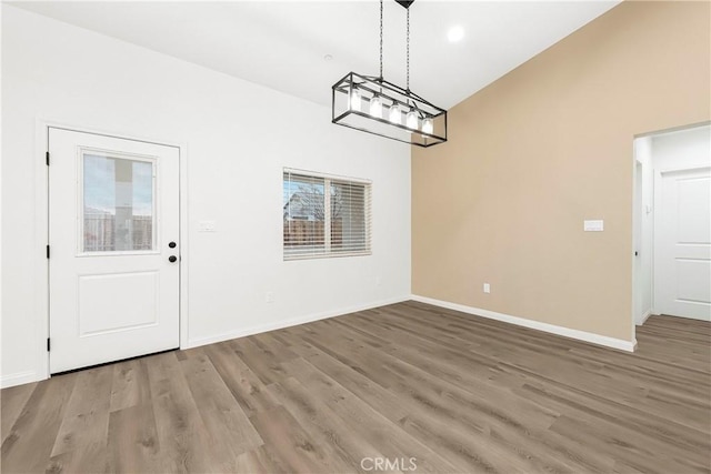 unfurnished dining area with baseboards, vaulted ceiling, and wood finished floors