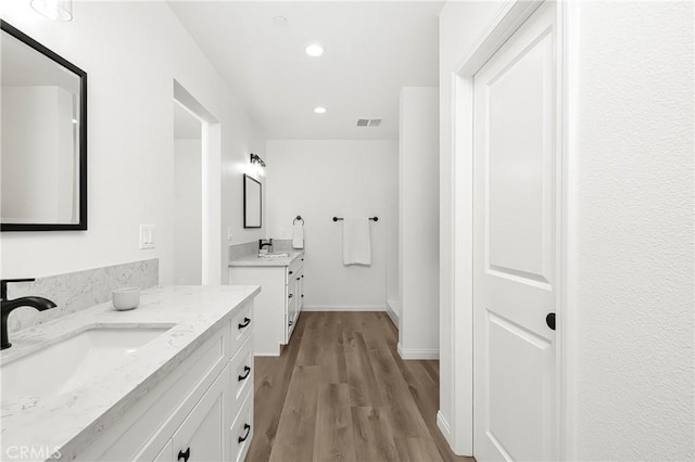 full bathroom featuring baseboards, two vanities, a sink, and wood finished floors