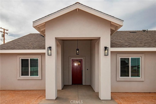 doorway to property featuring roof with shingles and stucco siding