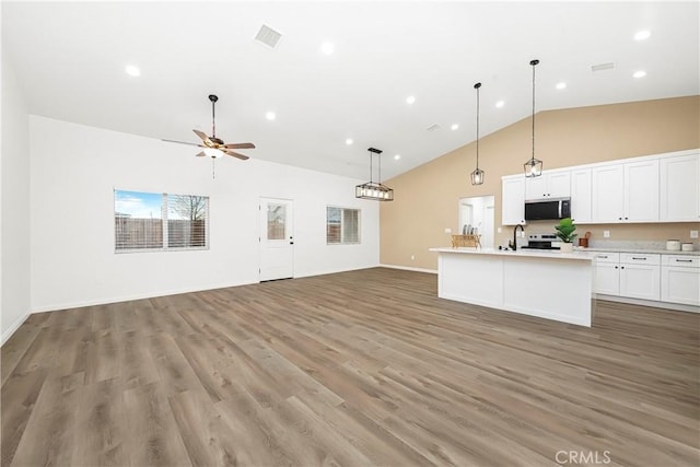 kitchen featuring light countertops, open floor plan, stainless steel microwave, and light wood finished floors