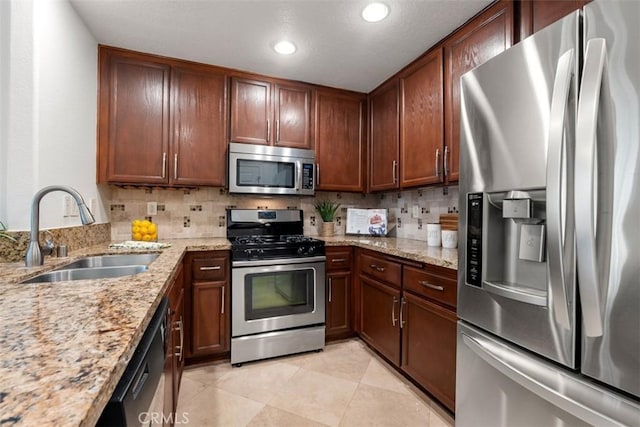 kitchen featuring light stone counters, backsplash, appliances with stainless steel finishes, and a sink