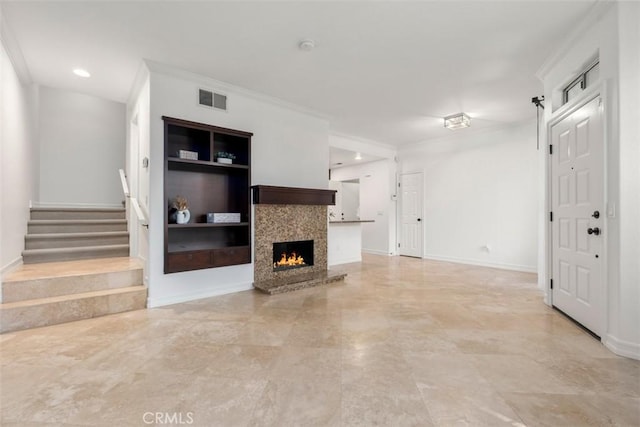 living area featuring visible vents, built in shelves, ornamental molding, a warm lit fireplace, and stairs