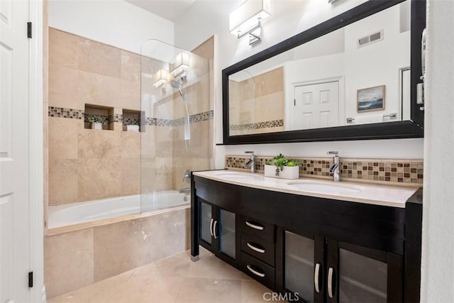 bathroom featuring visible vents, double vanity, a sink, tiled shower / bath, and backsplash