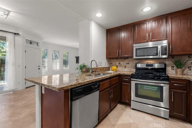 kitchen featuring backsplash, appliances with stainless steel finishes, a peninsula, and a sink