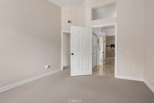 unfurnished bedroom with carpet flooring, baseboards, visible vents, and a towering ceiling