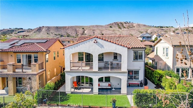 back of property with a fenced front yard, a patio area, a balcony, and stucco siding