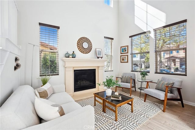 living room featuring a glass covered fireplace, wood finished floors, a towering ceiling, and baseboards