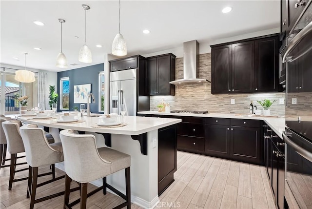 kitchen with stainless steel appliances, a kitchen breakfast bar, light countertops, backsplash, and wall chimney exhaust hood