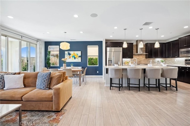 kitchen featuring open floor plan, light countertops, wall chimney exhaust hood, and built in appliances