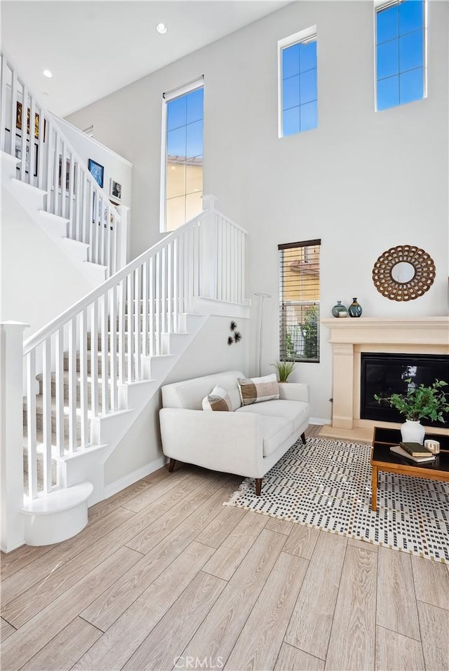 living room with stairway, a high ceiling, a glass covered fireplace, wood finished floors, and baseboards