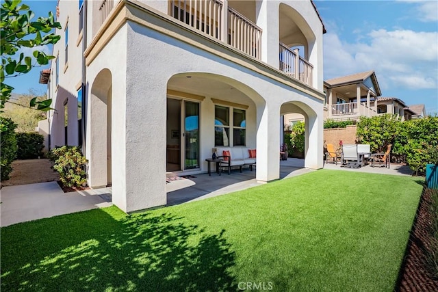 rear view of property featuring a patio area, a lawn, a balcony, and stucco siding