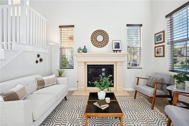 living room with a fireplace with flush hearth, wood finished floors, a towering ceiling, and baseboards