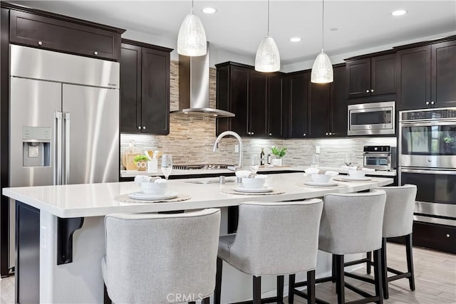 kitchen with built in appliances, light countertops, wall chimney range hood, and backsplash