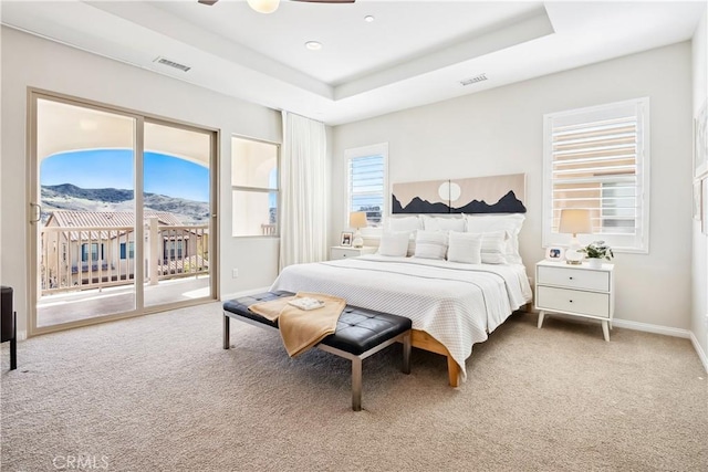 carpeted bedroom with a raised ceiling, visible vents, and access to exterior