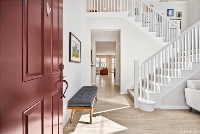 foyer featuring light wood-style floors, stairway, a towering ceiling, and baseboards