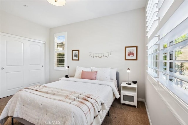 bedroom with a closet, dark carpet, and baseboards