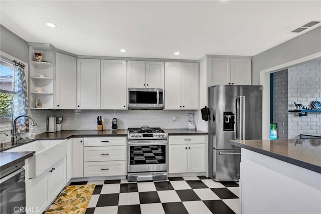 kitchen with stainless steel appliances, open shelves, a sink, light floors, and dark countertops